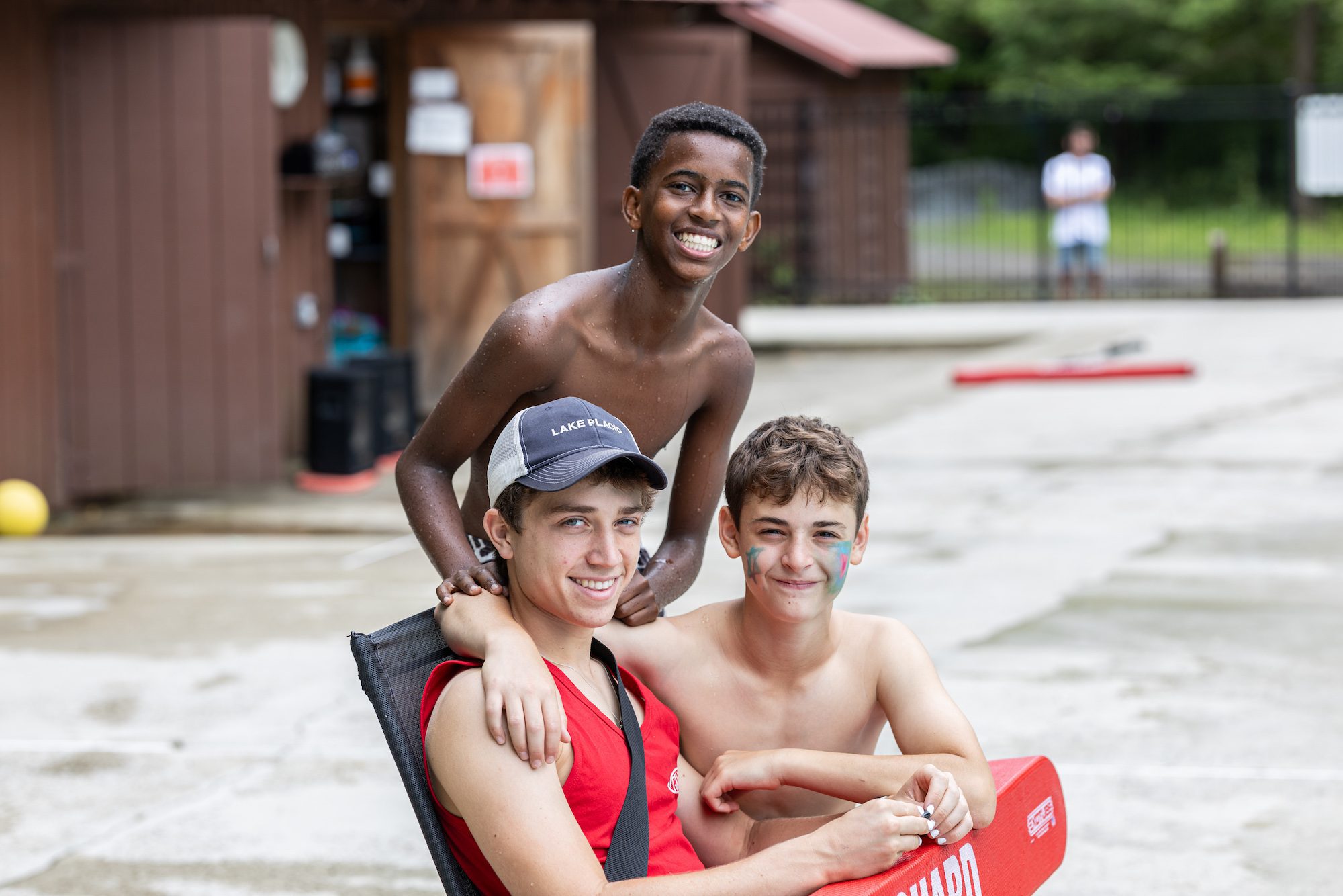 Two campers with a staff member on the pool deck smiling 