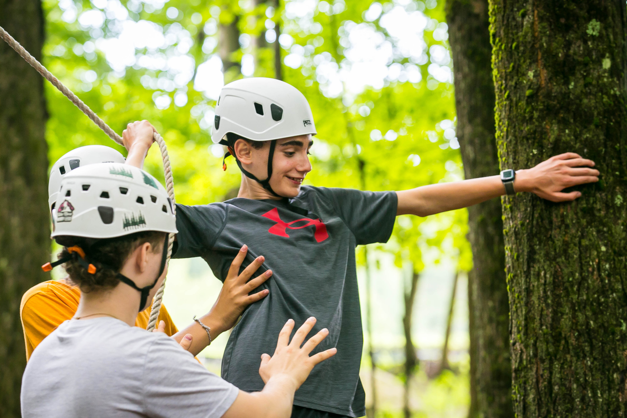 Camper on the ropes course being spotted and supported by another camper and staff member as they complete the challenge.